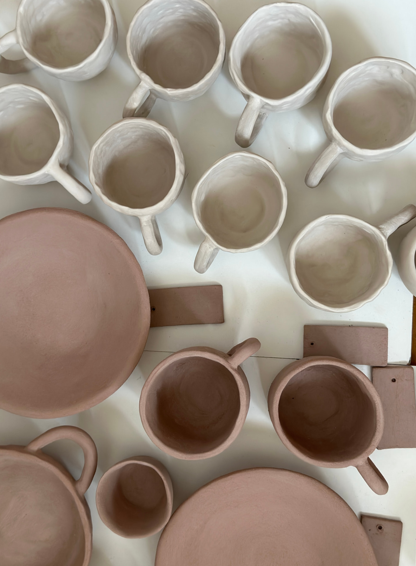 Piezas de cerámica en barro blanco y terracota secándose en el taller
